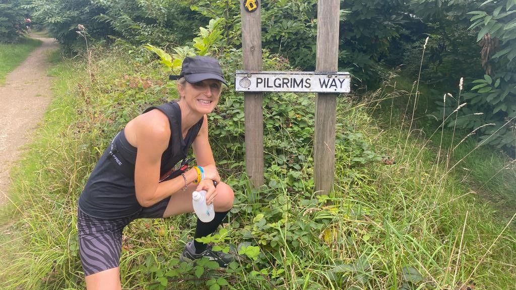 Sara Frow in running gear standing in front of a sign for Pilgrims Way 