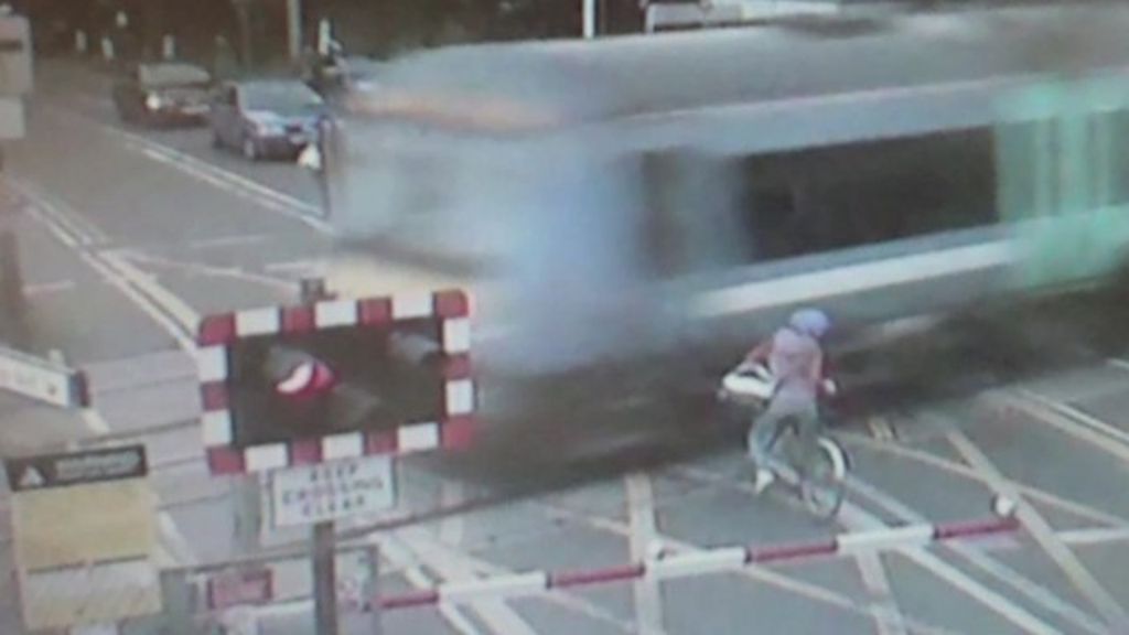 Woman on bike narrowly missing being hit by train at level crossing