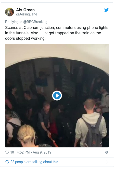 Twitter post by @AislingJane_: Scenes at Clapham junction, commuters using phone lights in the tunnels. Also I just got trapped on the train as the doors stopped working. 