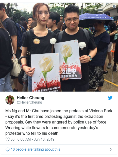 Twitter post by @HelierCheung: Ms Ng and Mr Chu have joined the protests at Victoria Park - say it's the first time protesting against the extradition proposals. Say they were angered by police use of force. Wearing white flowers to commemorate yesterday's protester who fell to his death. 