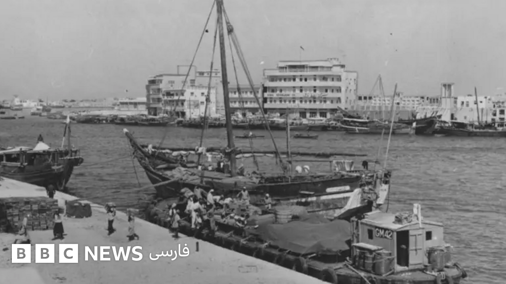 عکس سیاه و سفید از ساحل دوبی لنج‌ها در دو سوی آب کناره گرفته‌اند و باربران مشغول کارند