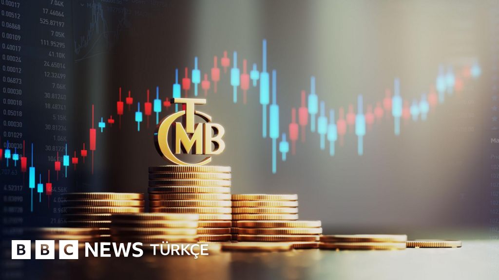madeni paralar üst üste dizilmiş üzerinde TCMB amblemi var hepsi altın rengi ve arkada borsa işlemleri var mavi ve kırmızı