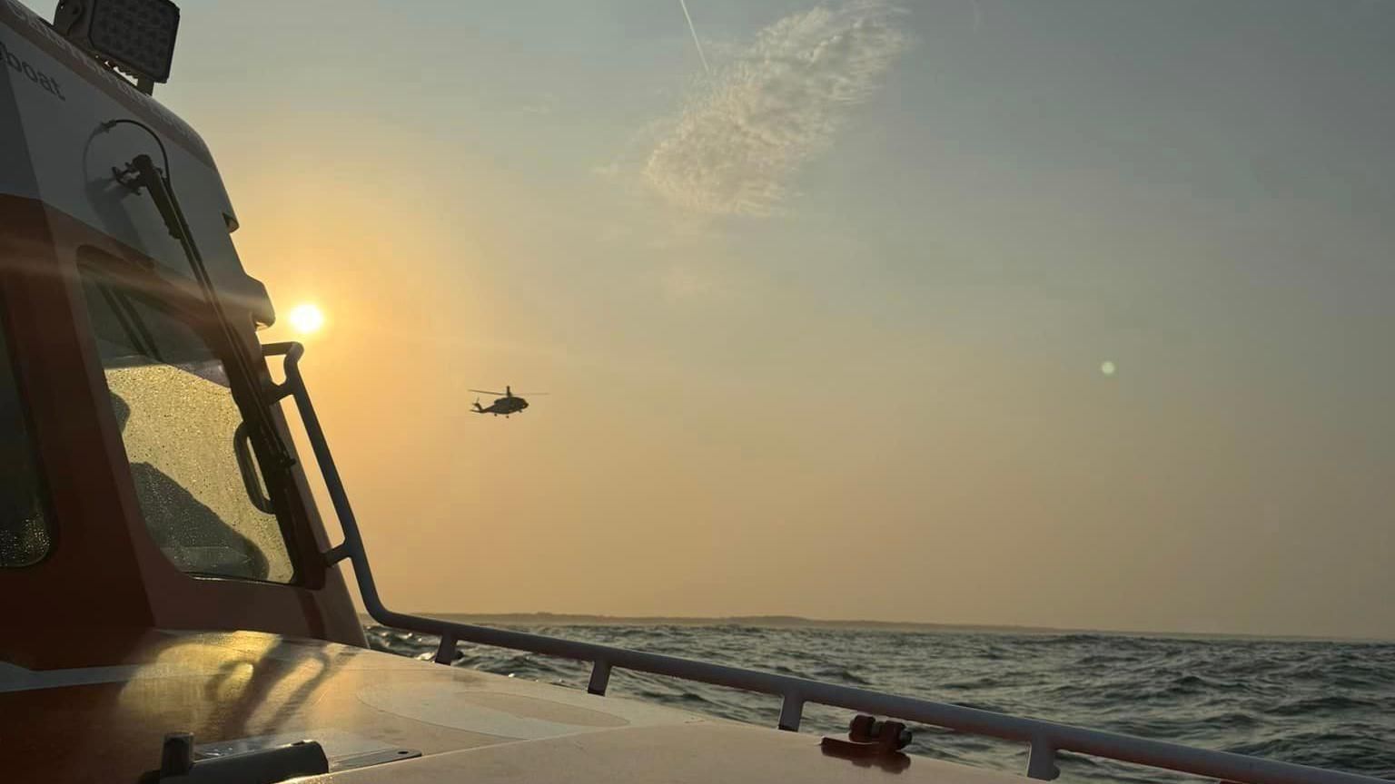 A photo taken from Caister Lifeboat of a Coastguard helicopter hovering above the sea and the sun in background