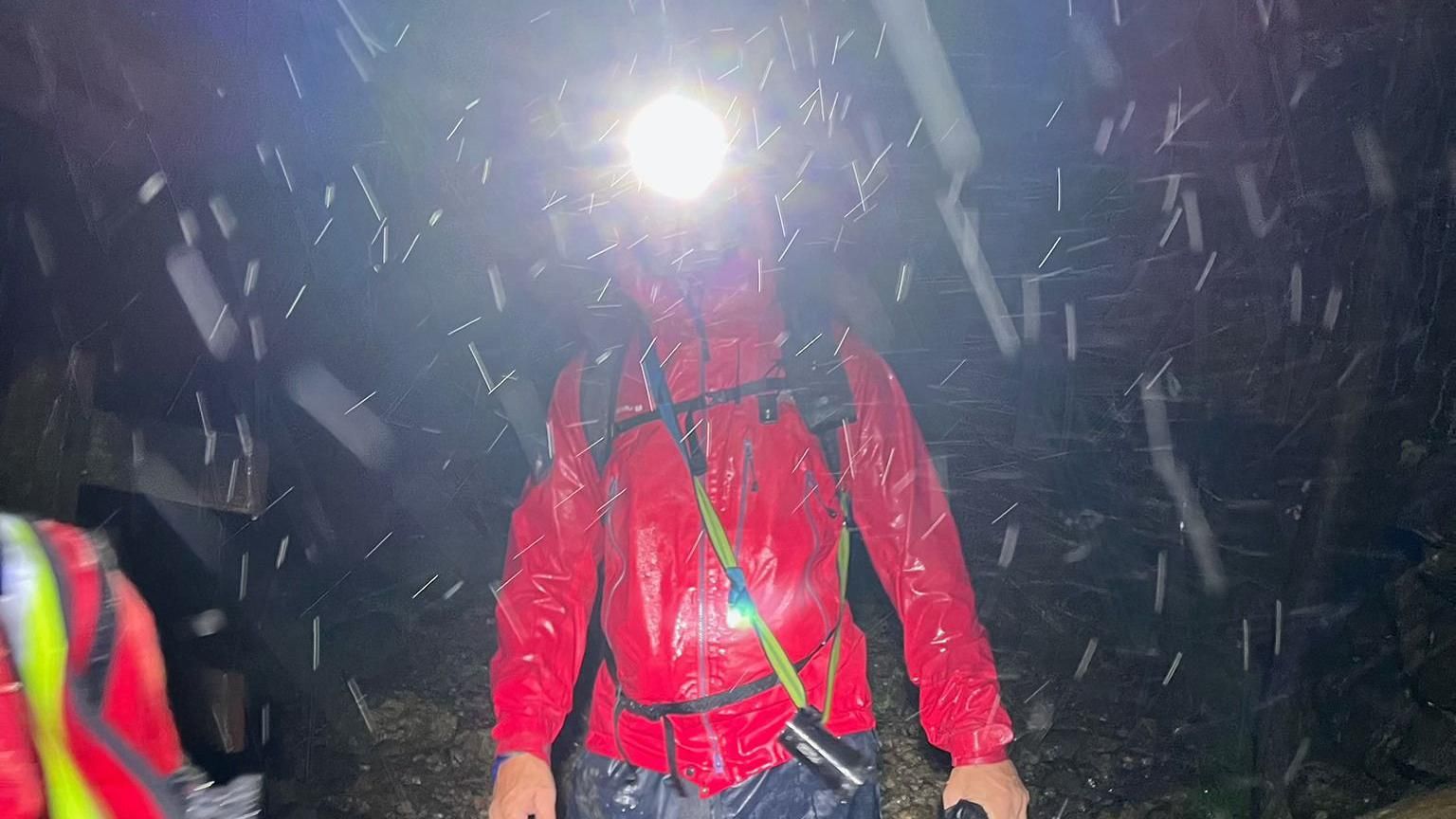 A mountain rescue volunteer wearing a headtorch and walking in heavy rain