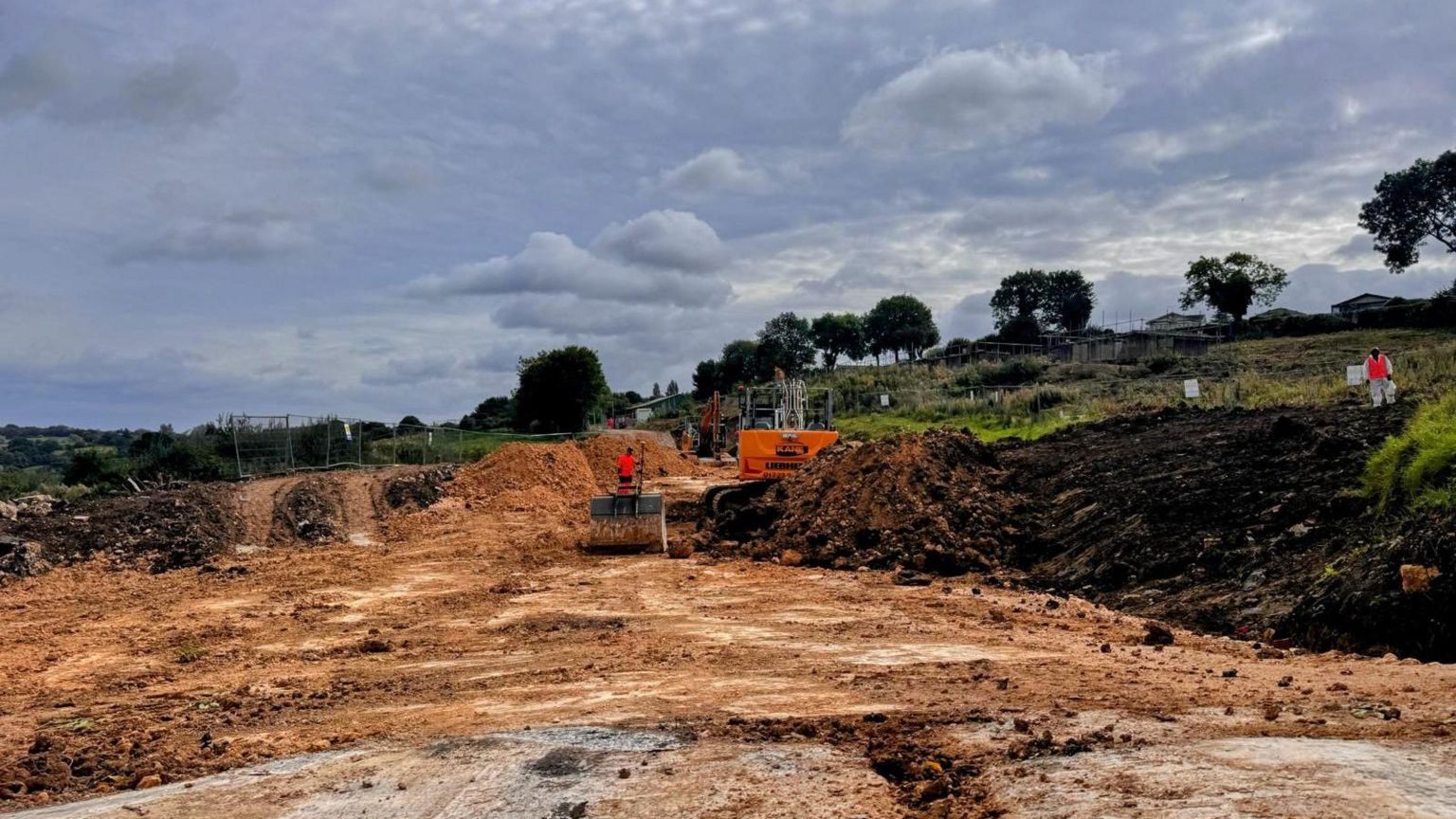 A building site with large mounds of earth, a digger and people in high-vis clothing