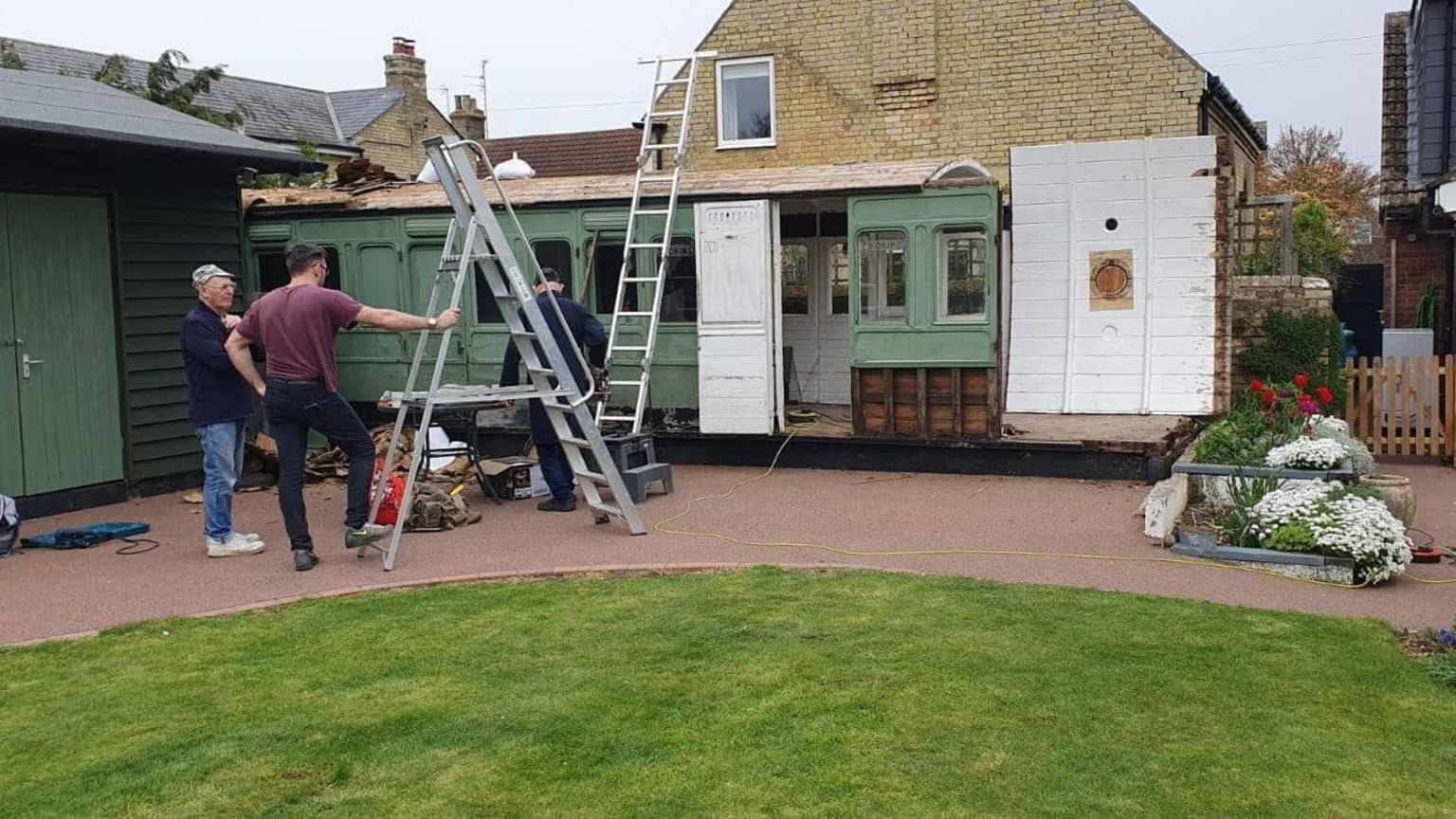 Picture of four people dismantling the green railway carriage in a back garden