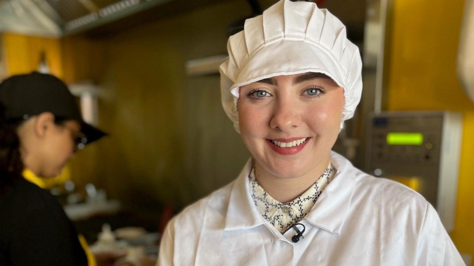 Nicola Carrington stands in a kitchen wearing white overalls and a white hat to cover her hair