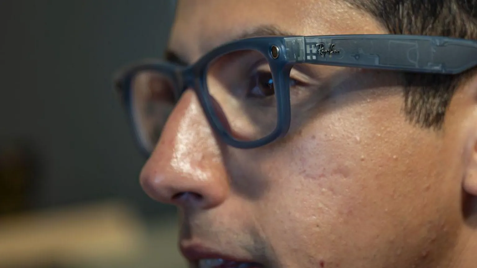 Getty Images Close-up profile of a person wearing translucent, dark grey Ray-Ban smart glasses featuring a small built-in camera lens near the hinge.