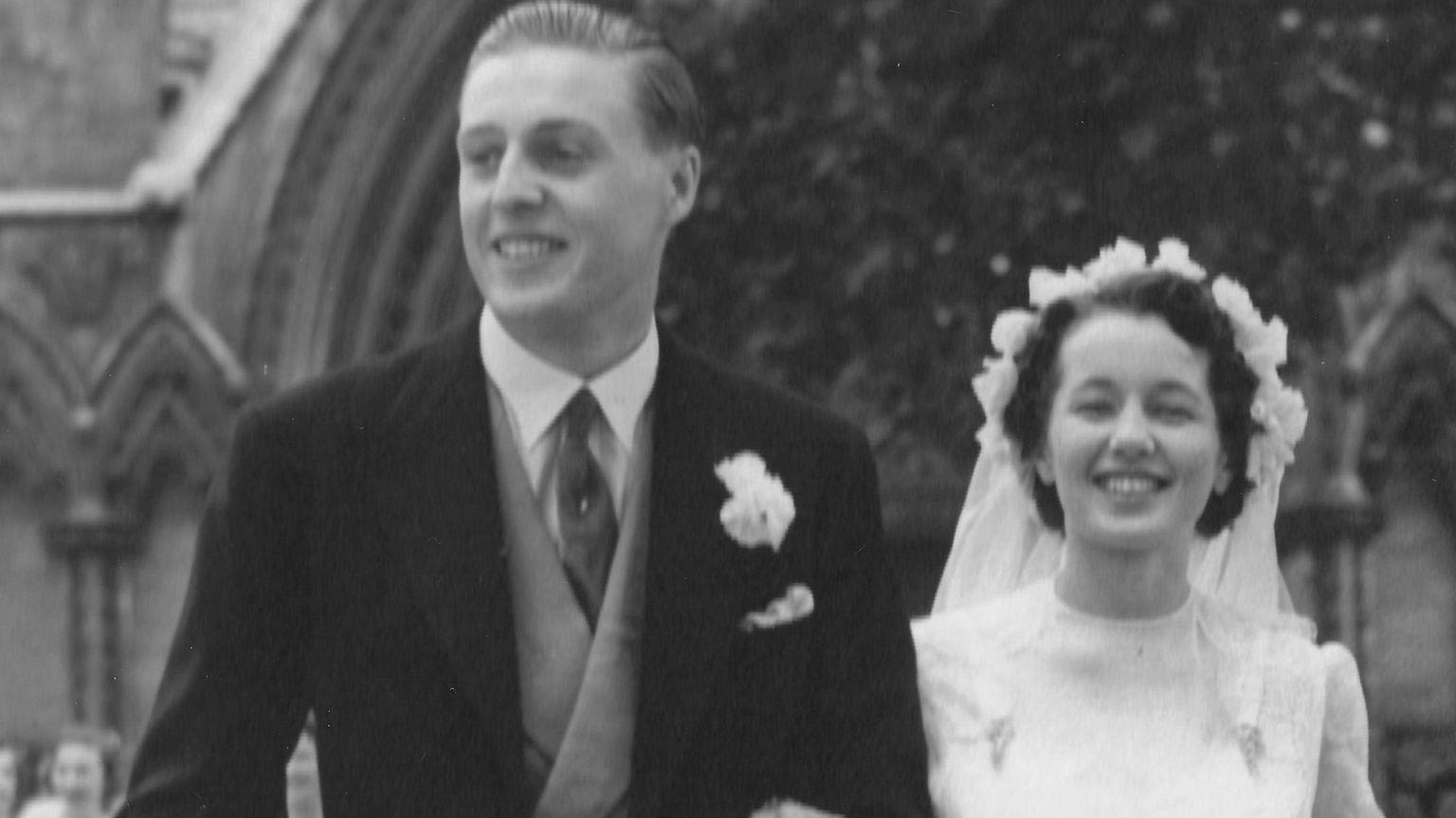 Bill and Cherry's wedding photo. Bill is in a traditional wedding suit and Cherry in a white dress and is wearing a white veil