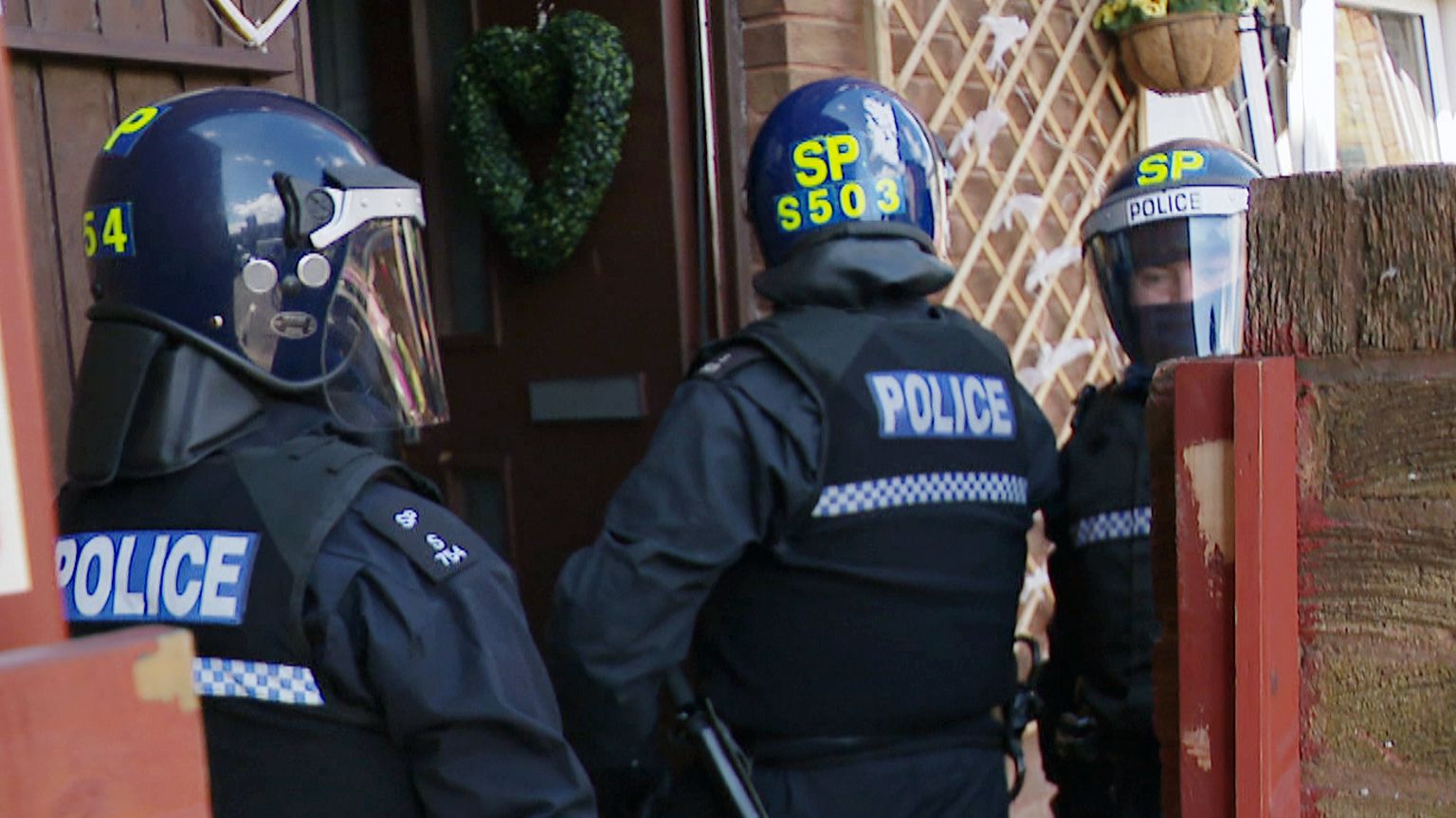 police in body armour and helmets at the door of a home