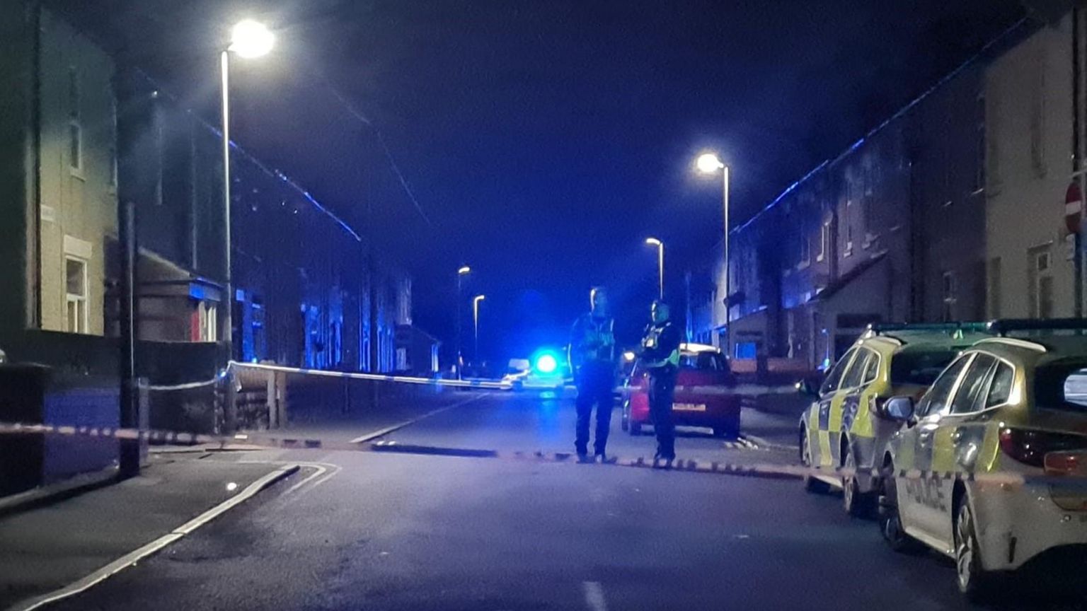 Parked police vehicles and a cordon with two police officers standing in the middle of the street