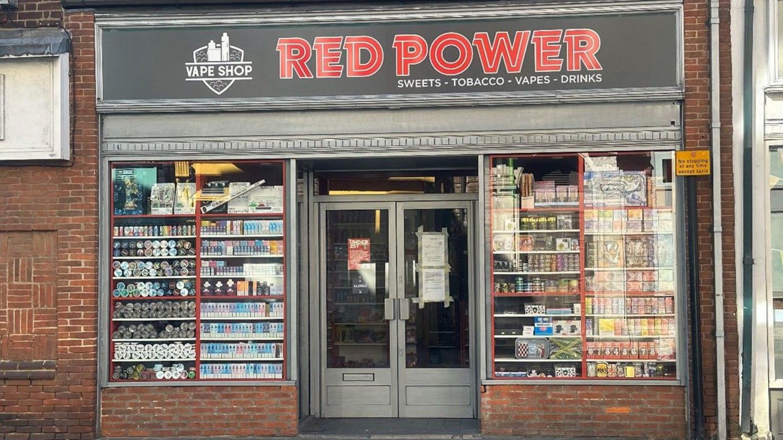 The storefront of Red Power vape shop. It is a red brick building, with the windows full of vapes and tobacco displays