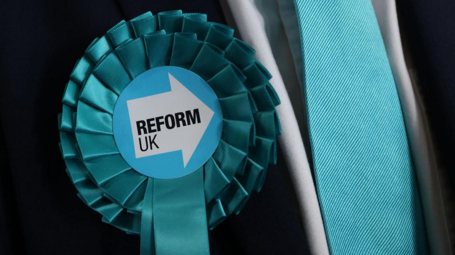 A stock image shows a Reform Party logo on a rosette on someone's chest