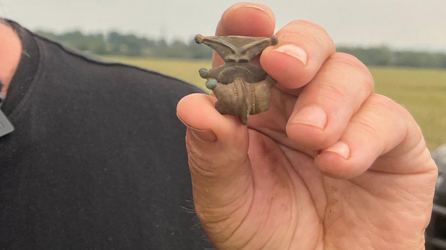 A hand holding a dirty but ornate brooch