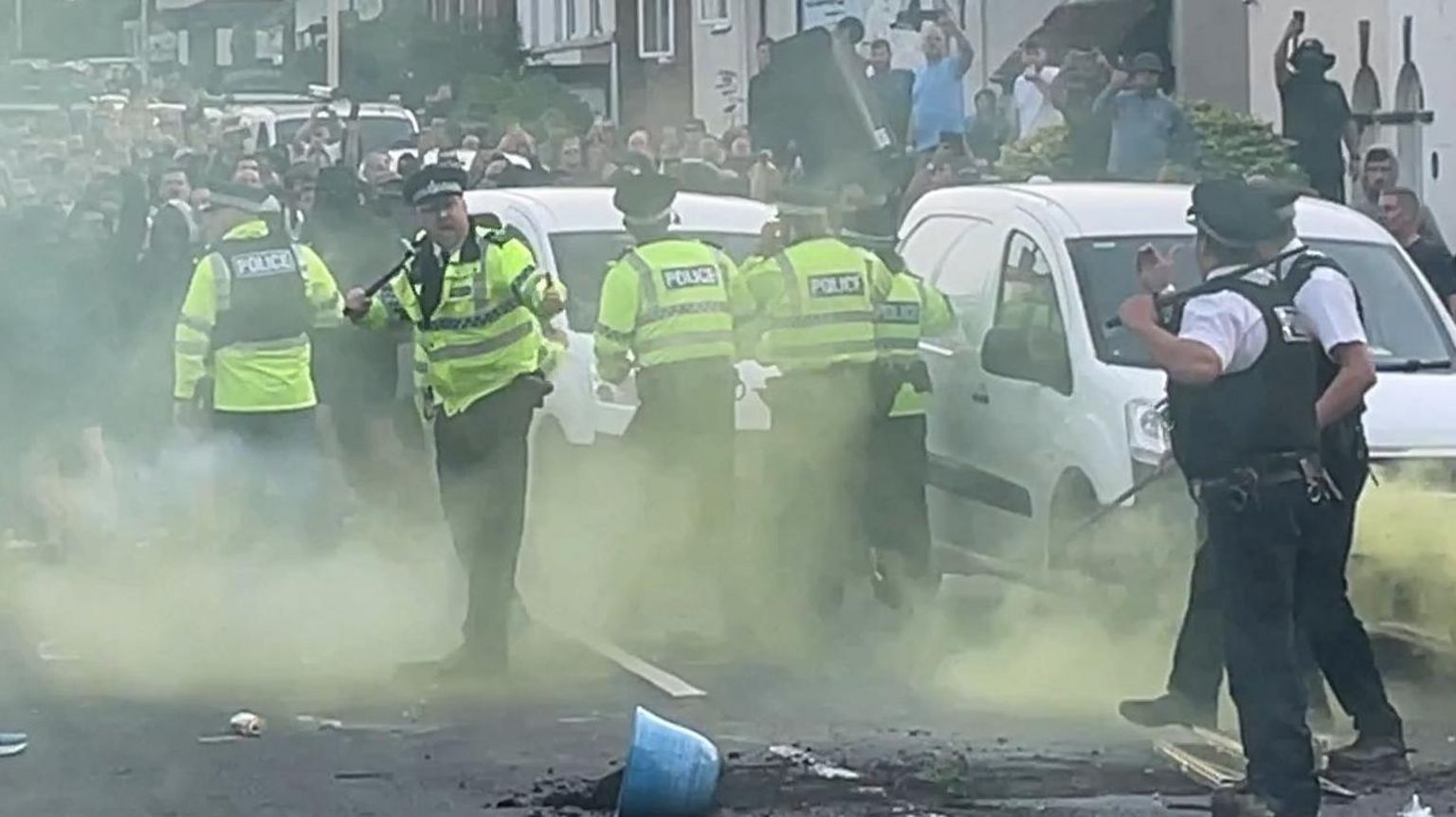 A large group of people confront police in a road in Southport