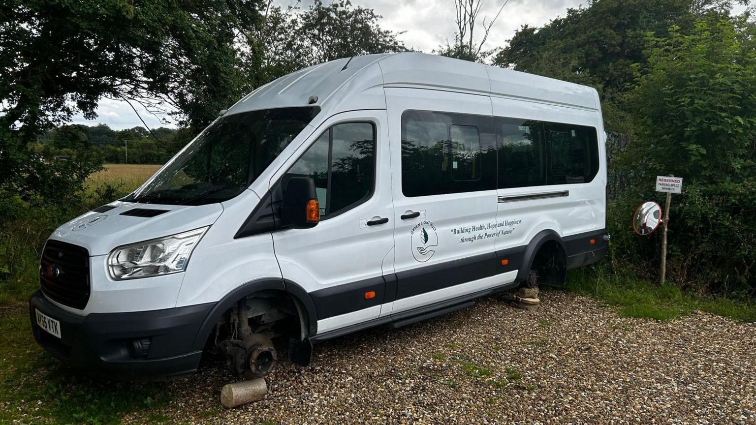 The white vandalised minibus with its wheels missing, and the wheel arches propped up on wooden stilts