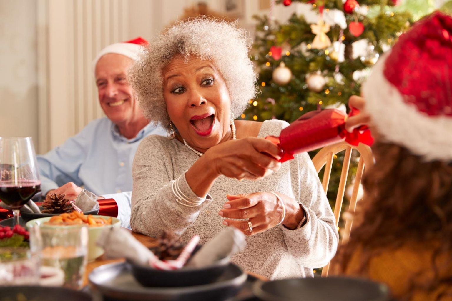 Бабушка тянет рождественский крекер с внучкой, когда они сидят за столом