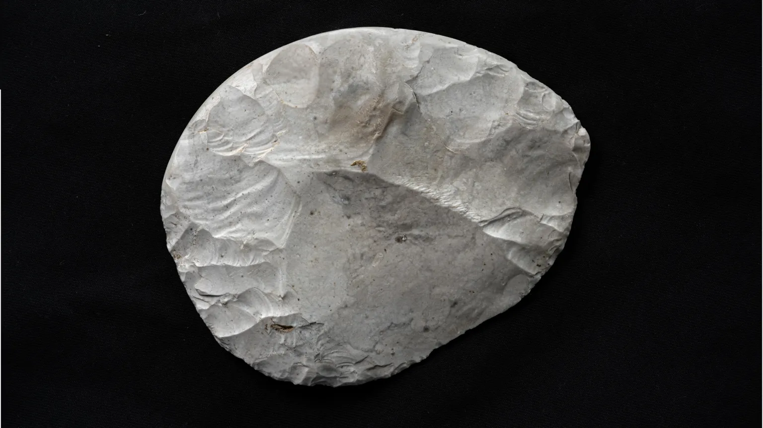 Tony Jolliffe/BBC News A rounded piece of flint that has been carefully worked to create a knife. It is white, with some brown and grey marks, and is set against a black background. The areas where pieces of the flint have been struck off using another stone are clearly visible. It is not a perfect circle but its sides are rounded.
