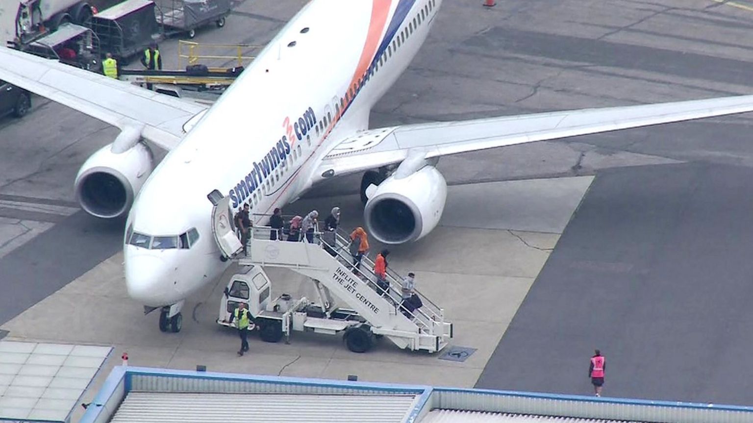 People walk down the stairs from a plane carrying evacuees from Sudan