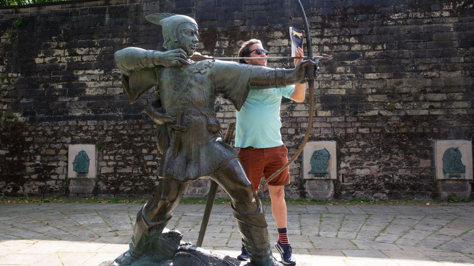 A man reading a book next to a Robin Hood statue