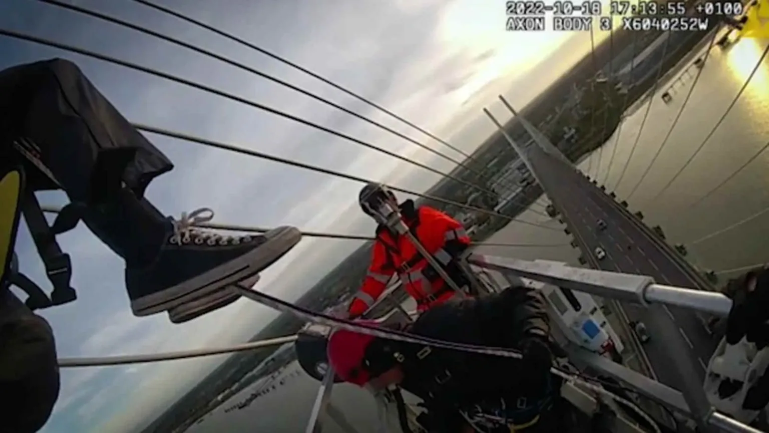 This body camera footage shows a person in a red high-visibility jacket positioned on what appears to be a large bridge structure. The image is taken from an elevated angle showing the bridge's cables, metal framework, and roadway below. The timestamp indicates it was recorded on October 18, 2022.