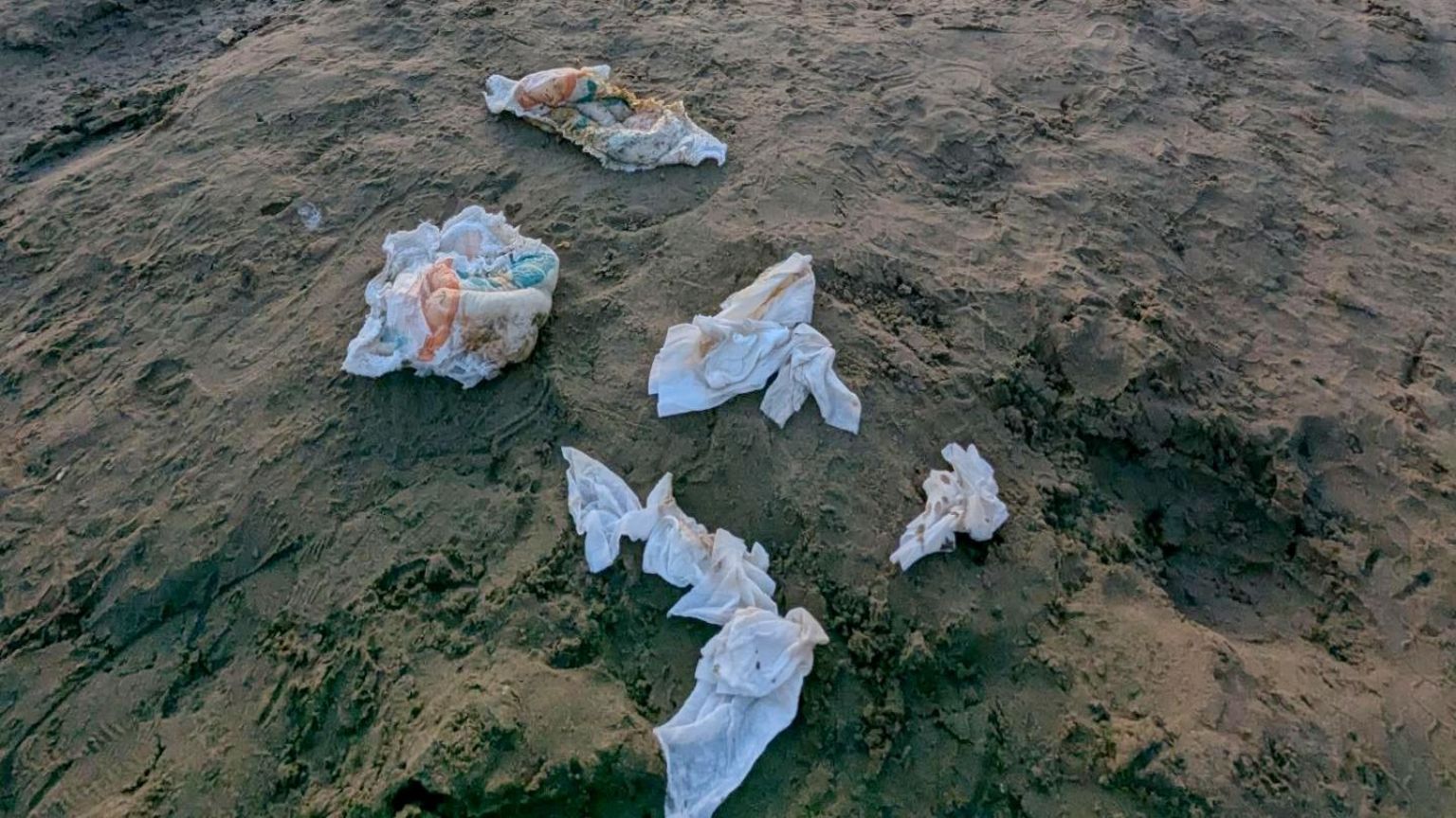 Three dirty nappies scrunched up and thrown on the sand. There are also dirty baby wipes beside them