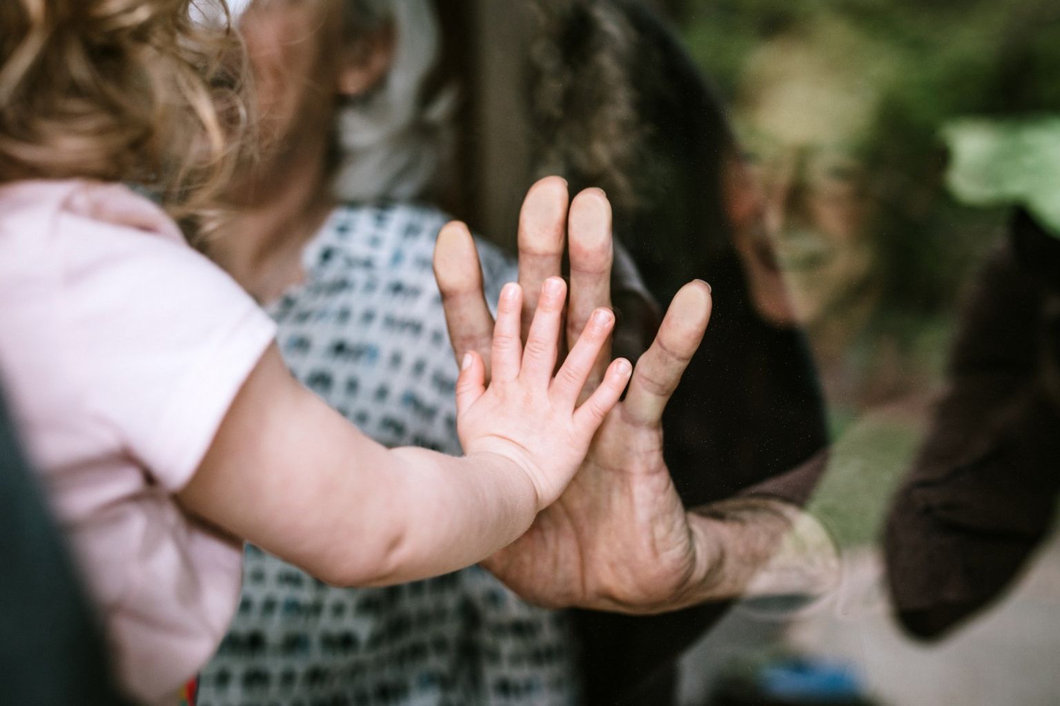 A toddler and an elderly person touching hands through glass