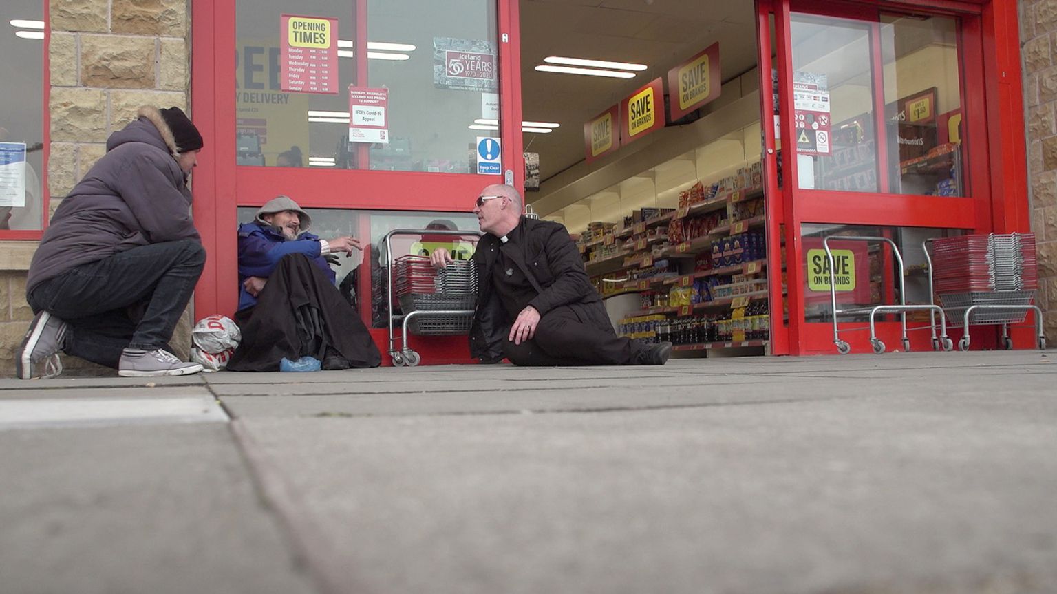 Pastor Mick Fleming talks to a man on the ground outside a shop