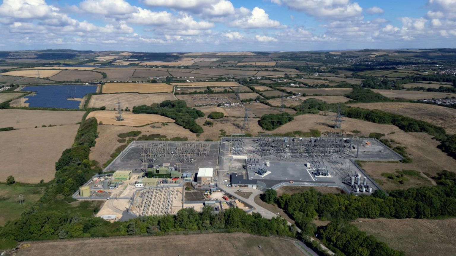 an aerial shot of an electricity sub-station. There are fields surrounding it.