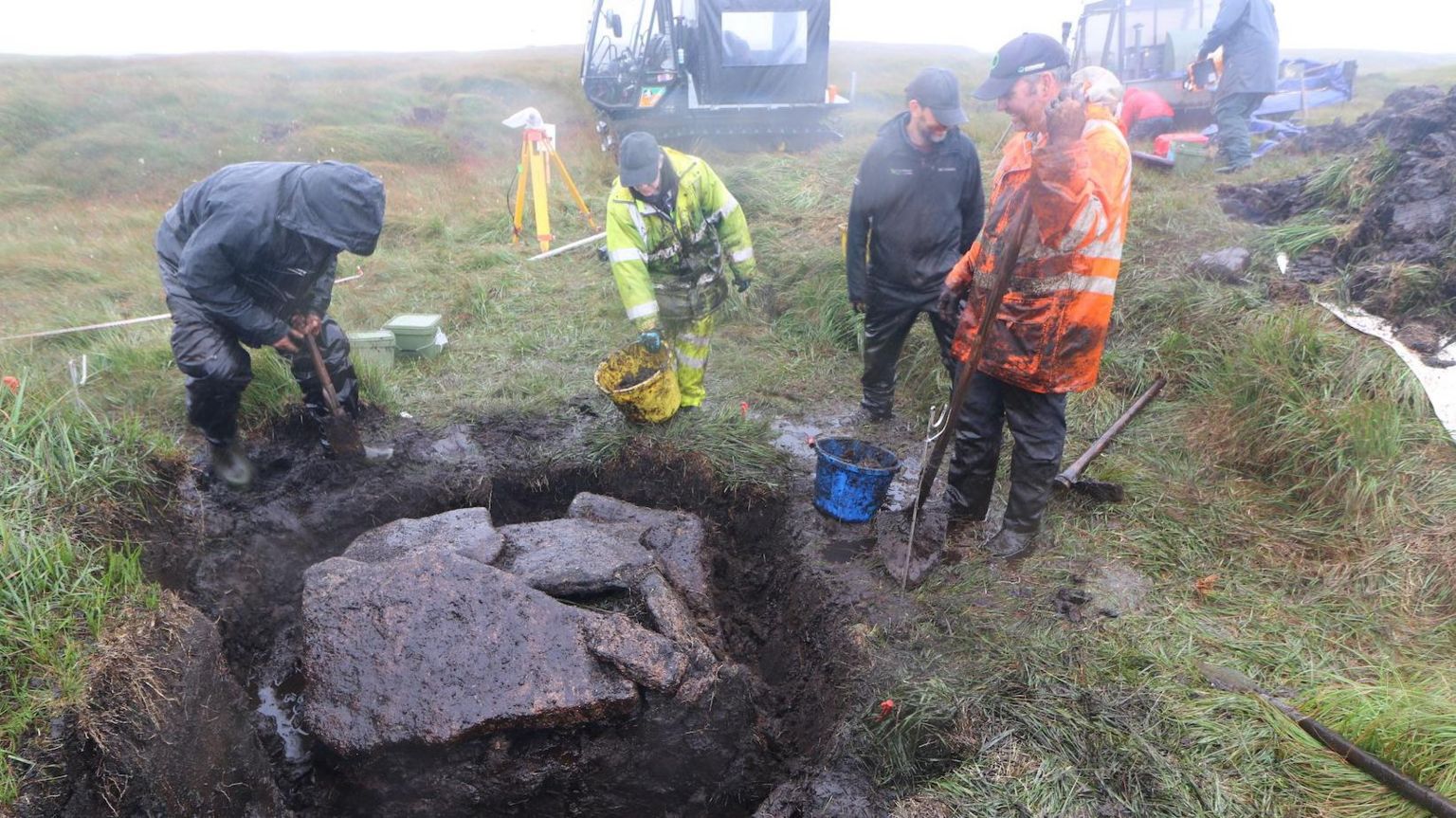 A team of four excavators stand over a large hole filled with rocks on a damp and misty Dartmoor landscape