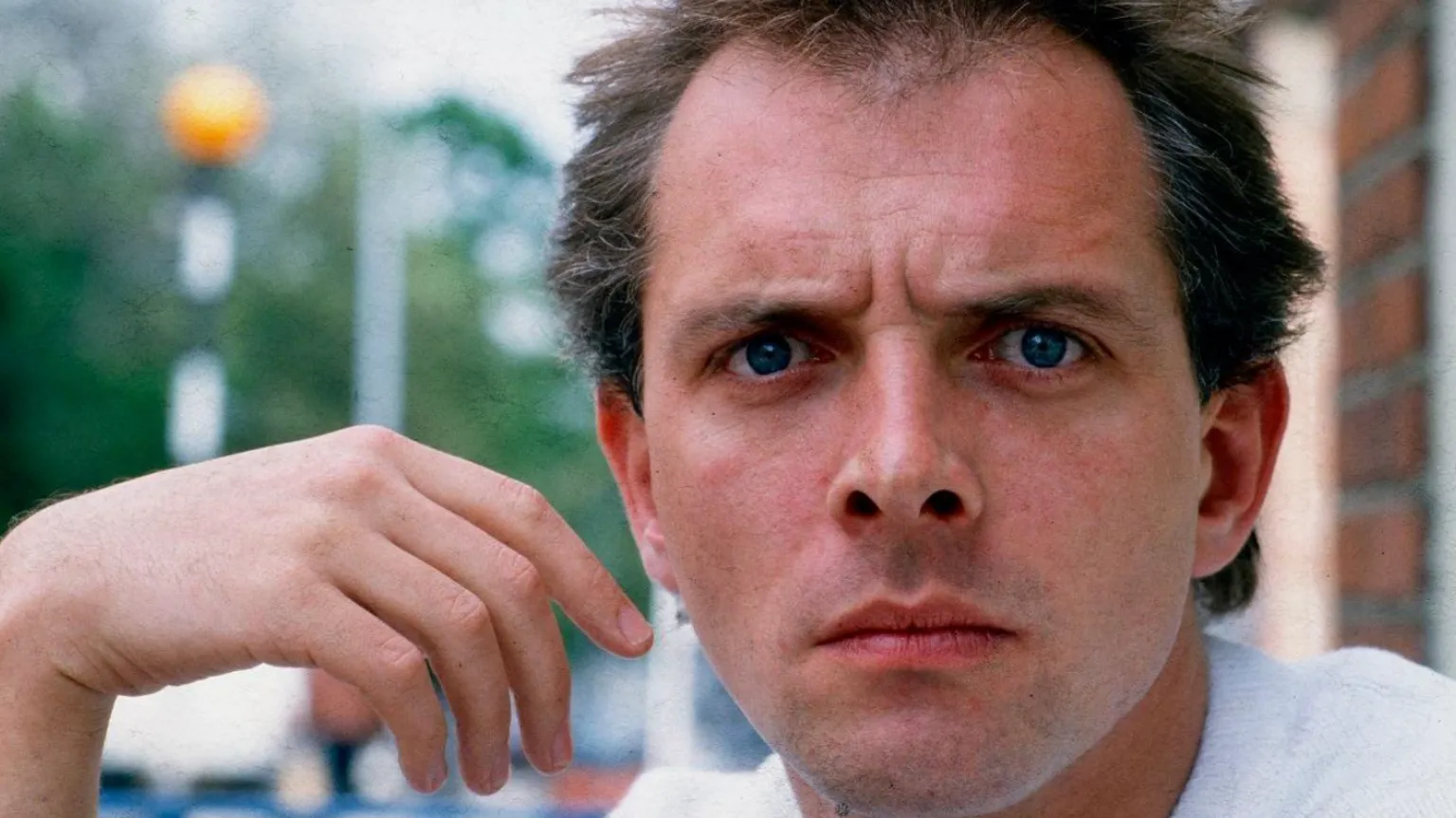 Getty Images Mayall, a clean-shaven man with dark hair, looks at the camera. His hand is raised and hangs limp by the side of his face. The background is blurred.