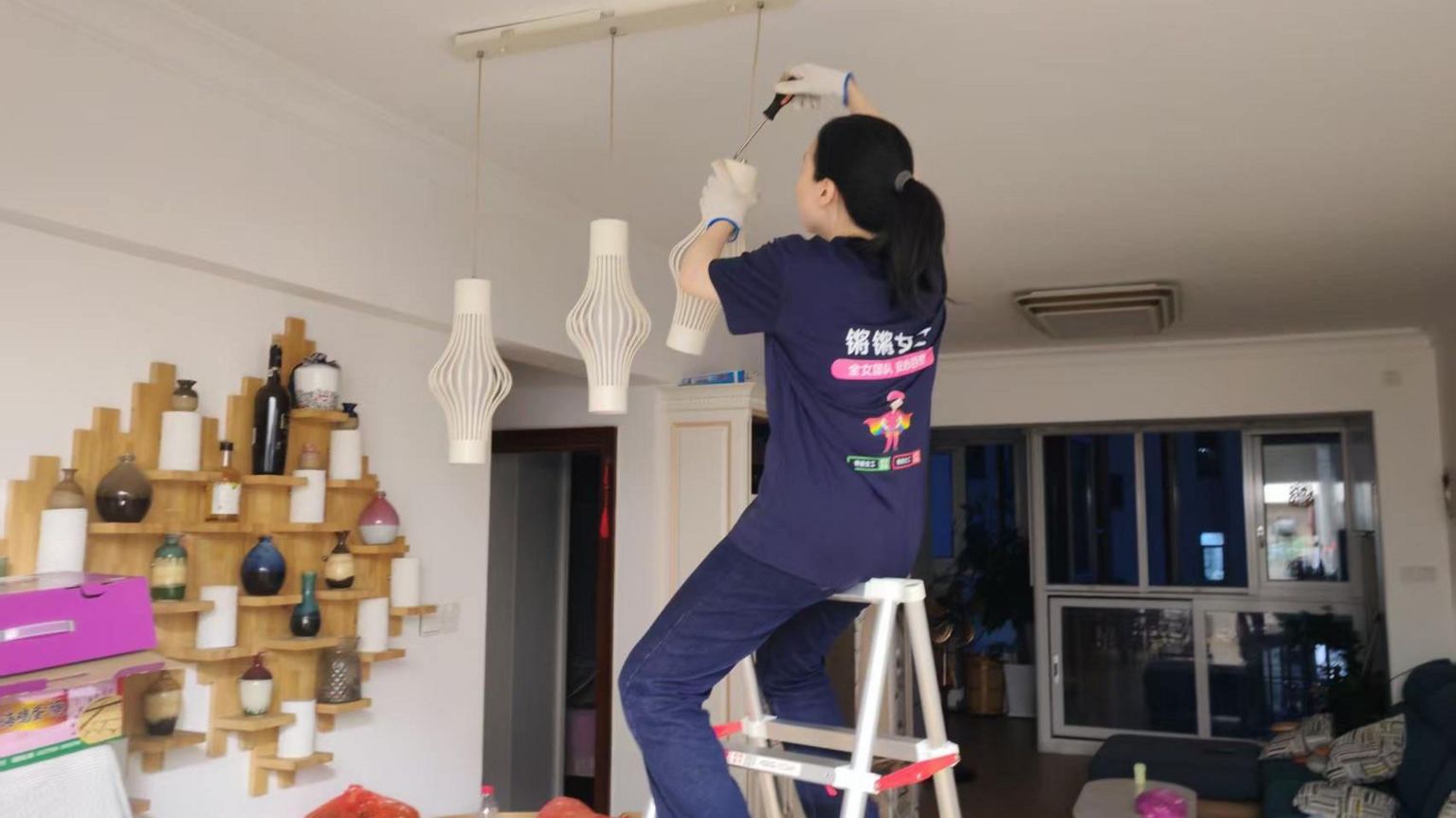 一位女性坐在梯子上,手拿螺丝刀拆卸灯胆