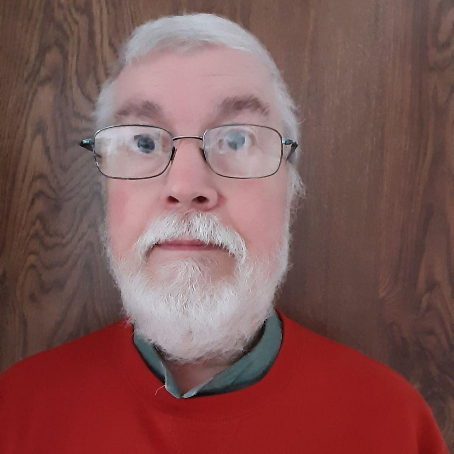 A man with grey hair and a grey beard, wearing a red jumper.