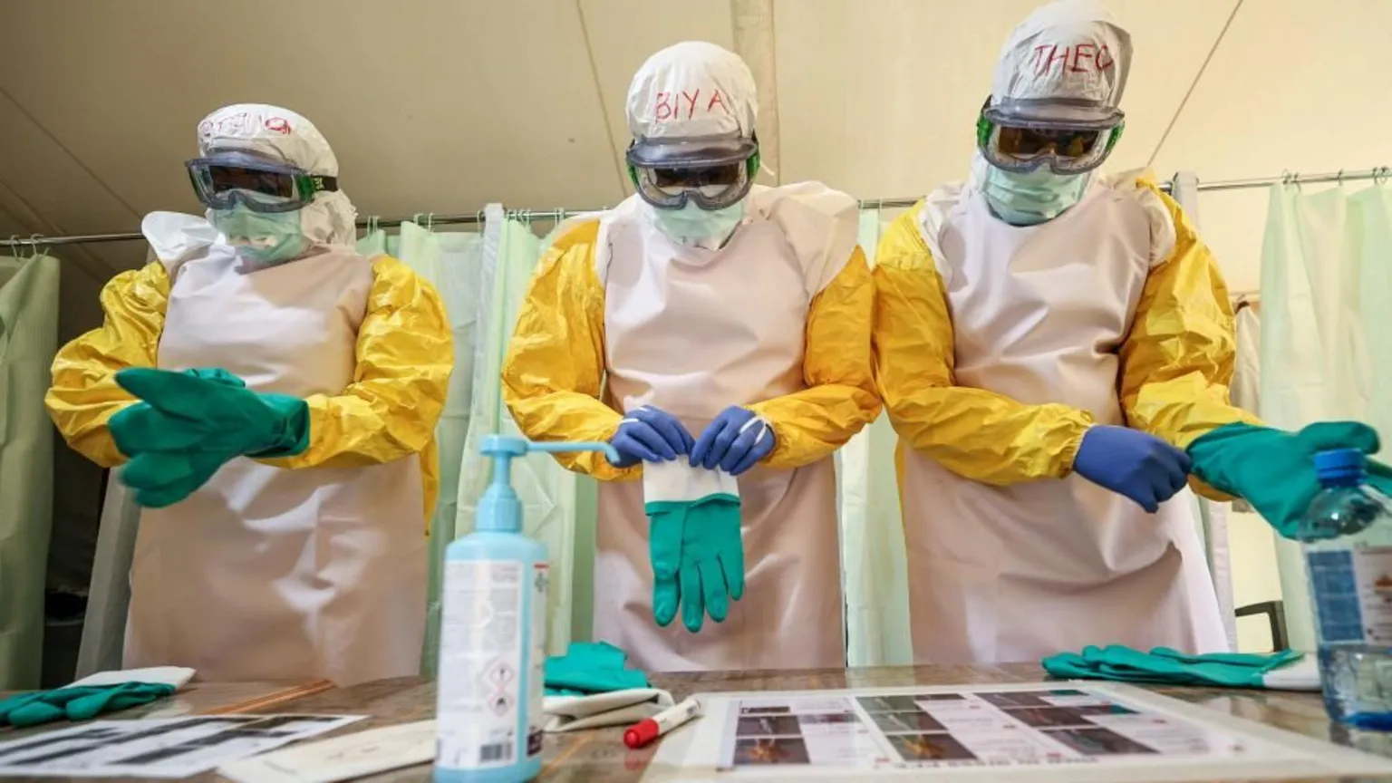 EPA Three health workers stand side-by-side as they put on full PPE. They are wearing goggles and protected by yellow and white overalls and are pictured putting on green gloves.