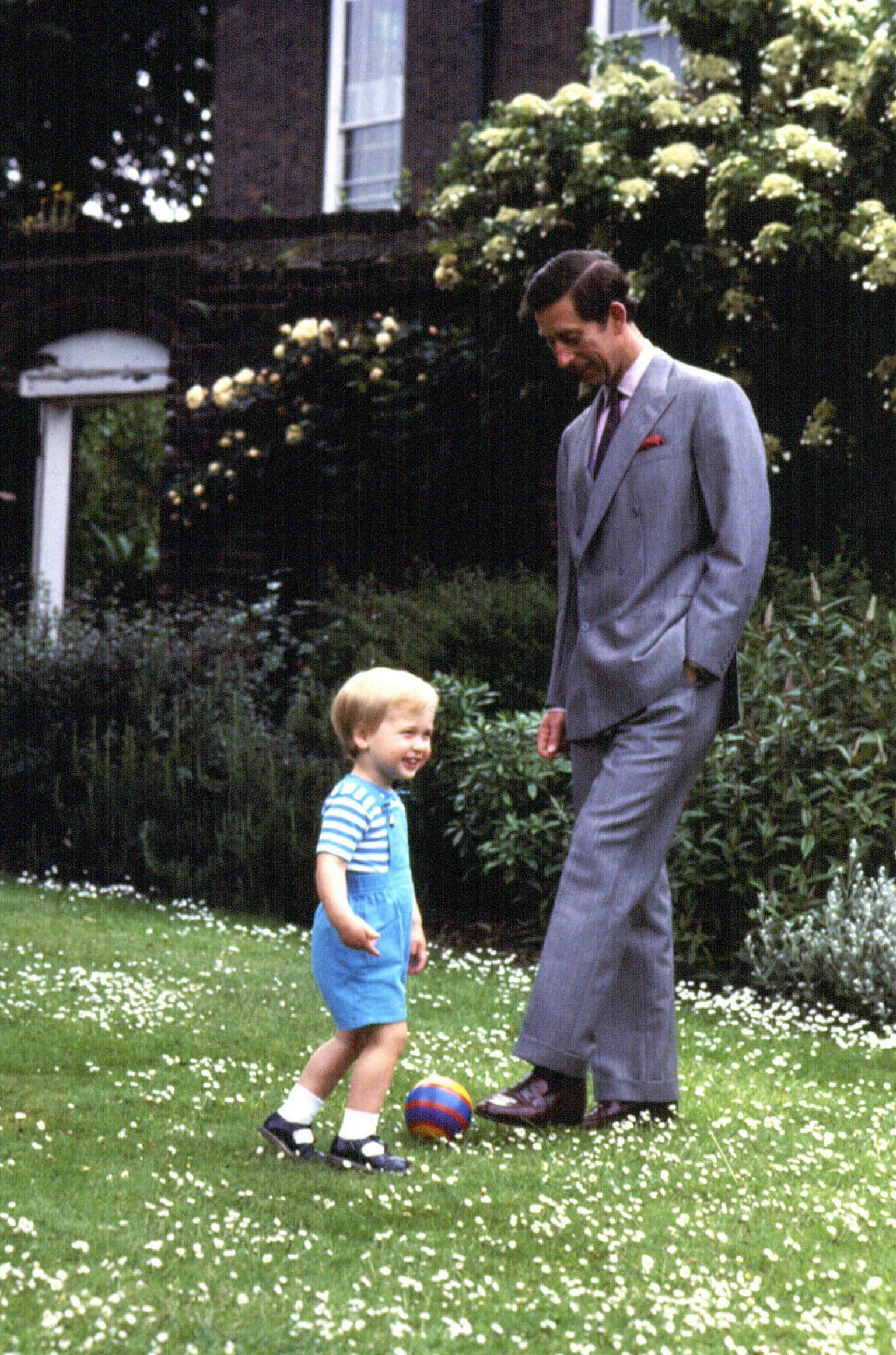 Young Prince William and young King Charles III kicking small football round in the garden