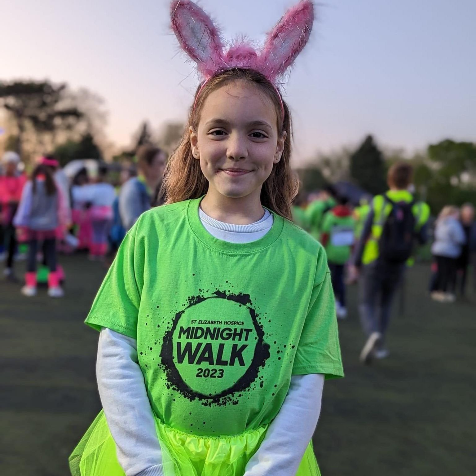 Harli, a 10 year old girl, with a bright green running top with St Elizabeth Hospice branding. She is also wearing bunny ears.