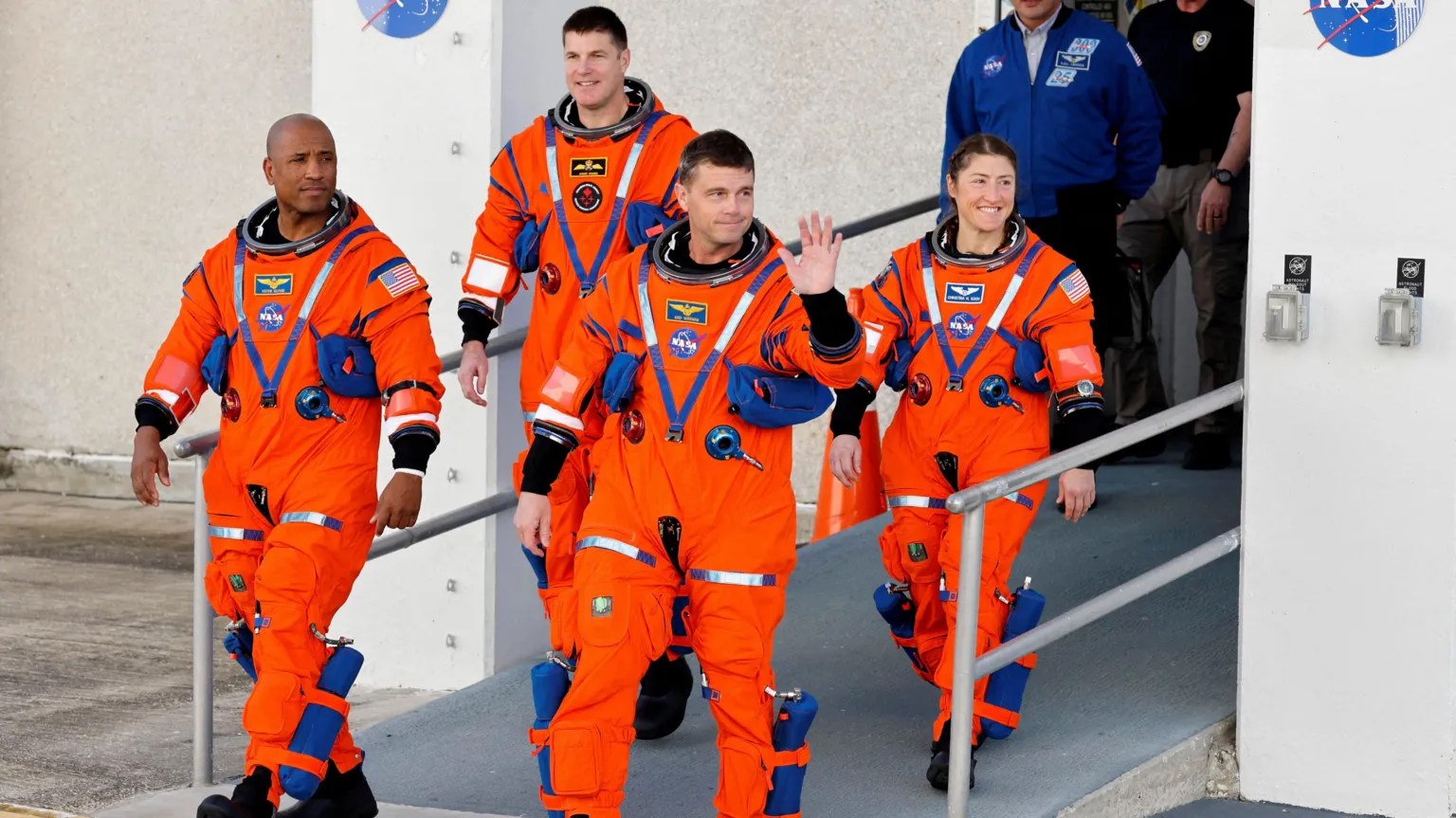 NASA The four Artemis II astronauts, in bright orange spacesuits, walks out of a Nasa building. From left to right they are Victor Glover, Jeremy Hansen, Reid Wiseman and Christina Koch. Reid Wiseman is raising a hand in a friendly wave.