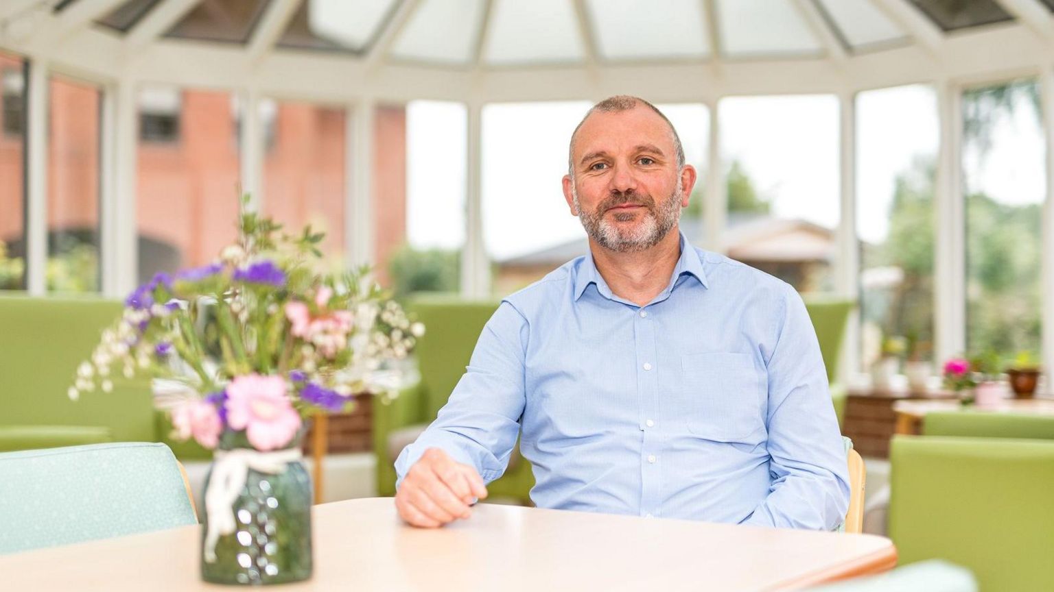 CEO Simon Fuller sitting at a table in a conservatory at the hospice with a vase of flowers in front of him
