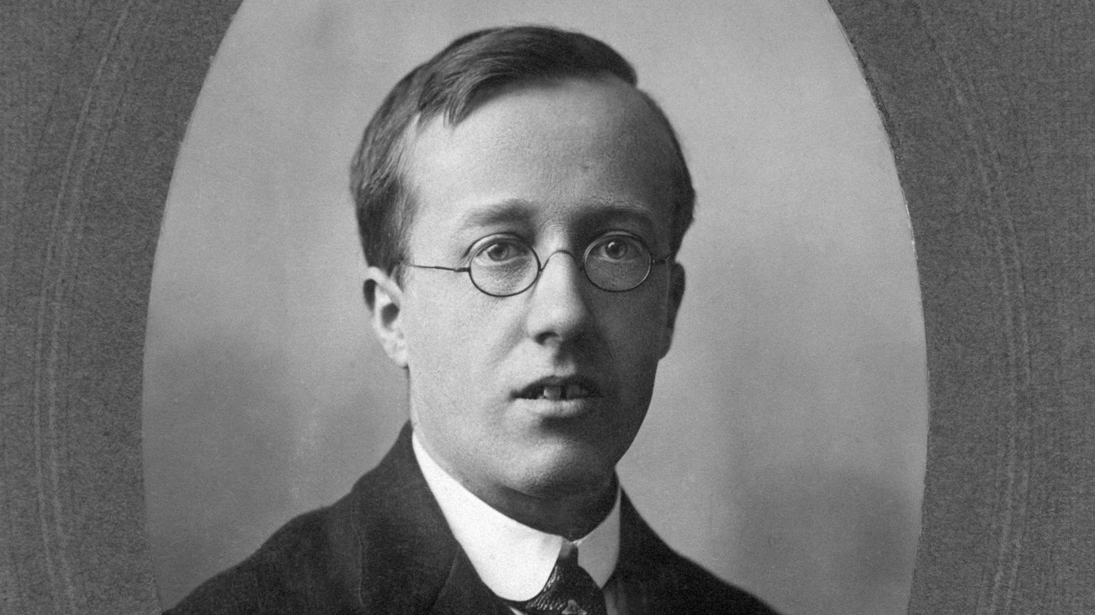 Black and white portrait of Gustav Holst. He is wearing a suit and tie and glasses