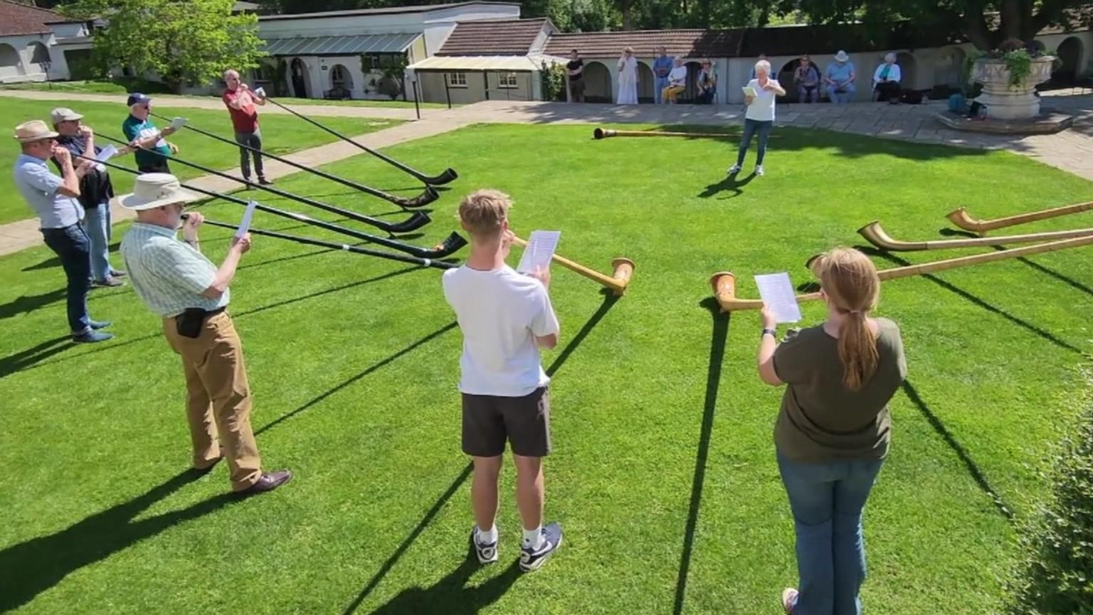 Circle of people playing alpine horns on a lawn