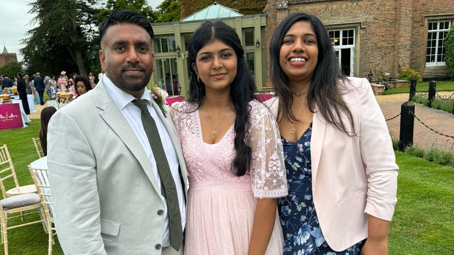 Tony Varghese wearing a suit while standing with two women at the wedding venue