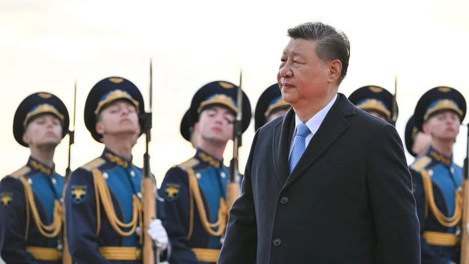 習近平穿著黑色外套和淺藍色領帶，站在俄羅斯士兵前面