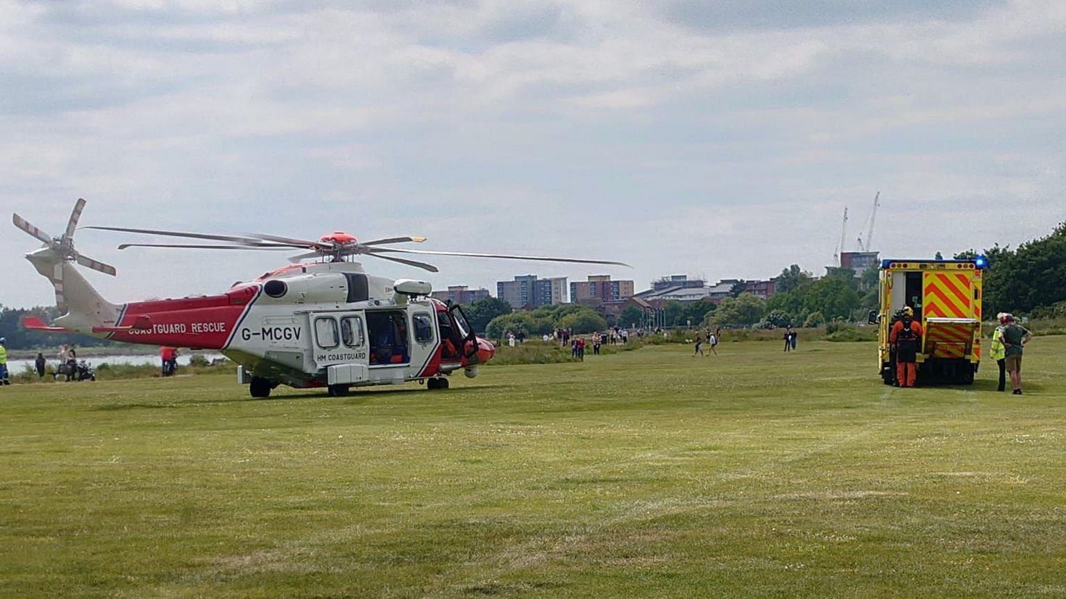 Red and white coastguard helicopter and an ambulance on a field with the sea in the background