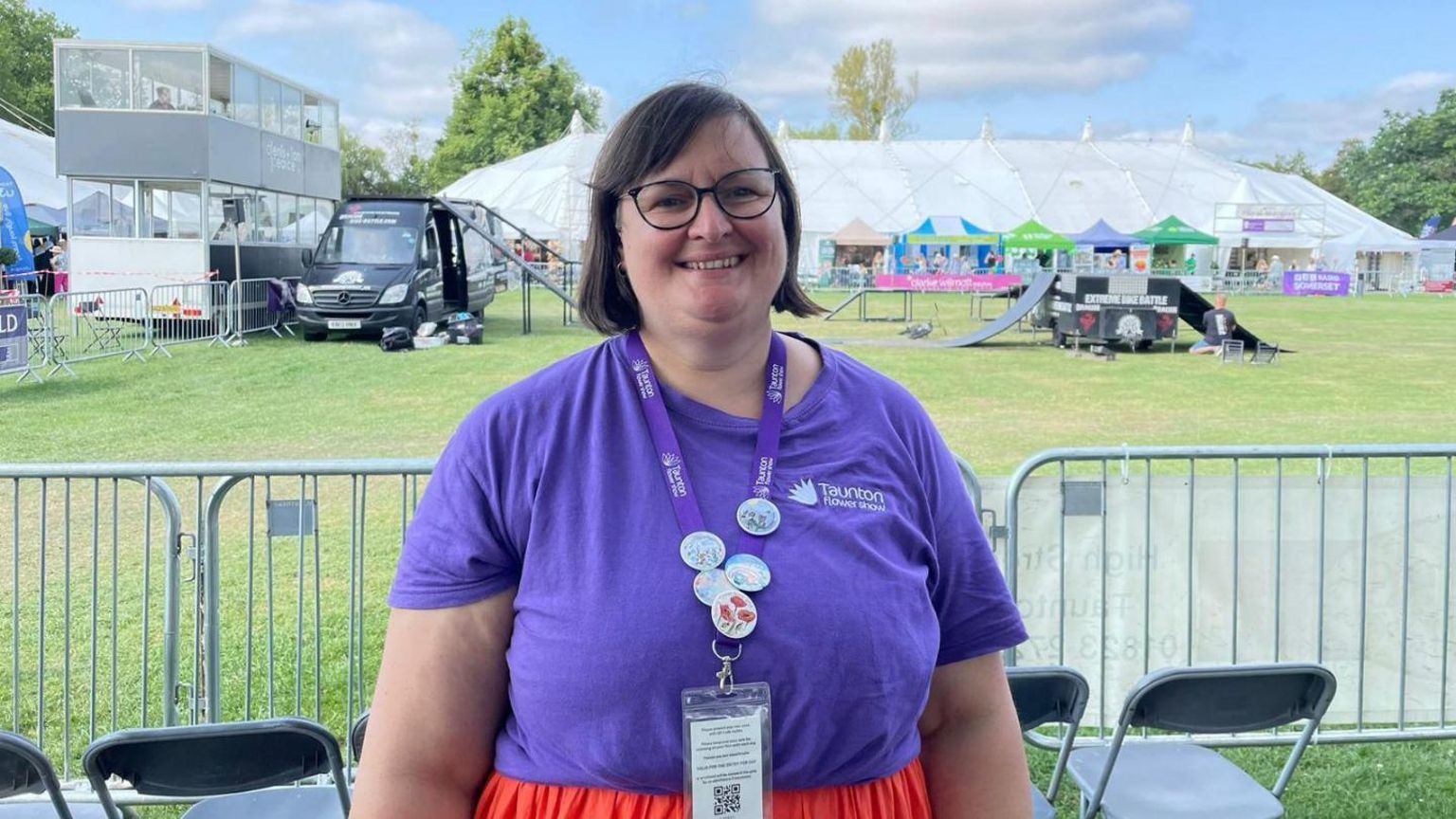 Becky Fox wearing a purple t-shirt and red shorts standing in front of a marquee at the flower show