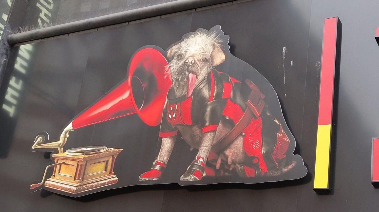 A close-up image of the HMV dog and gramophone logo, with the traditional dog replaced by Peggy in her red and black Deadpool outfit, on the sign of a store in Oxford Street, London's image