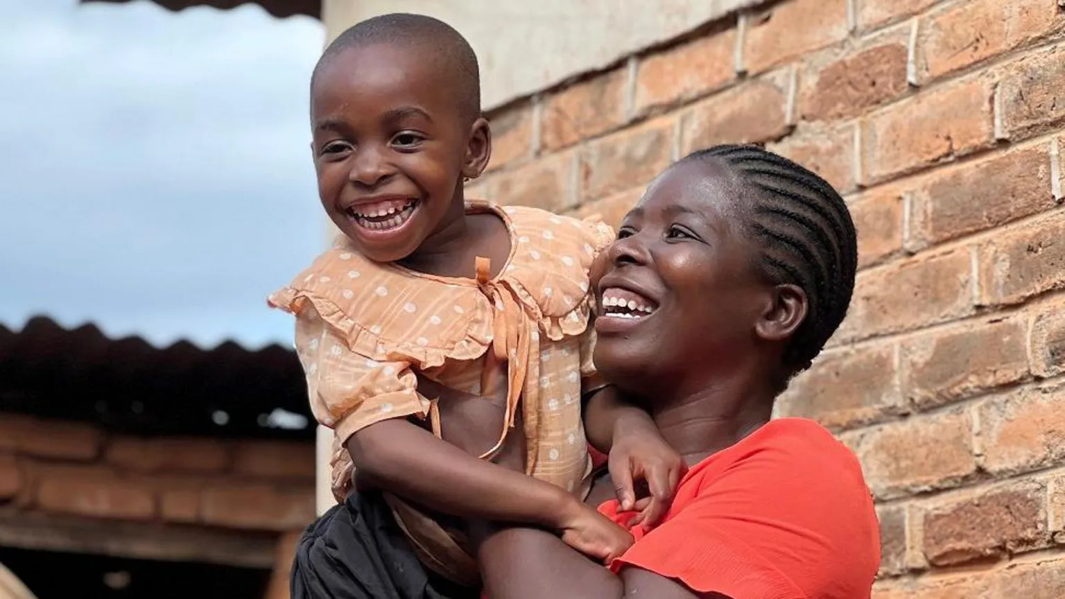 Martha Ongwane holding her daughter Rachael, both smiling during a quiet moment at home in Mzuzu, Malawi
