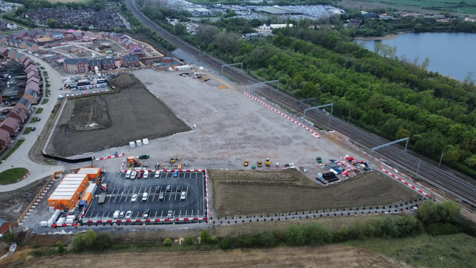 Ant Saddington/BBC Aerial view of a construction site with scattered equipment and vehicles. Nearby are residential houses and a railway track.