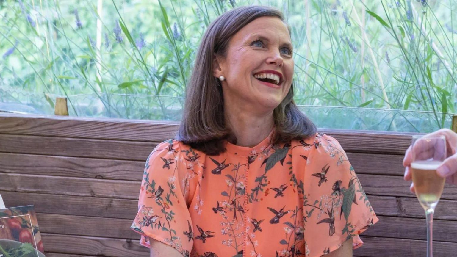 Maria sitting in a garden on a bench wearing a floral dress smiling