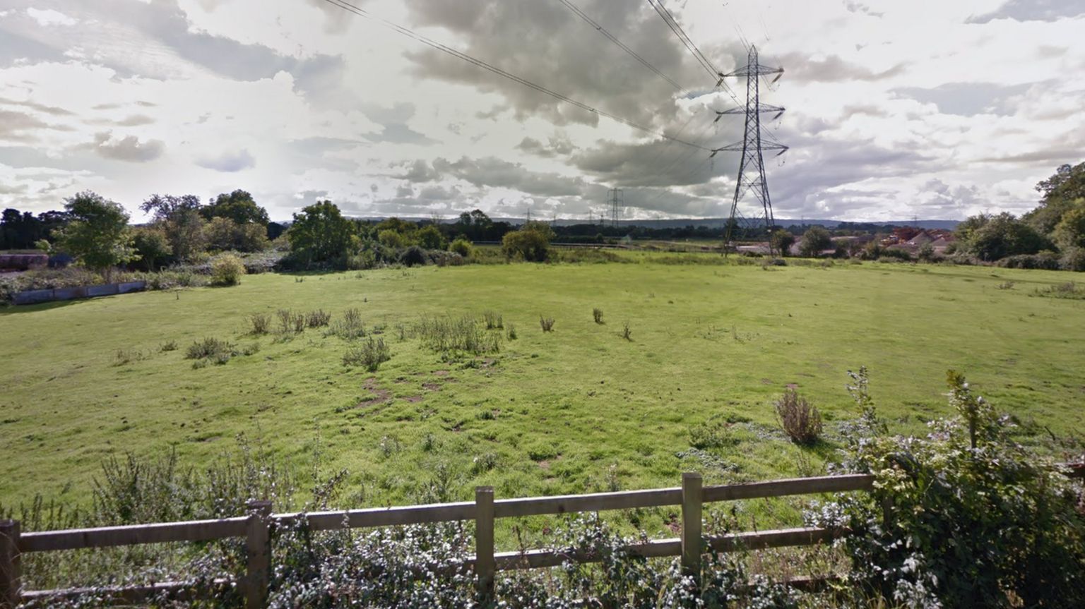 An open view of a field where houses might be built looking away from the road towards the distant railway line