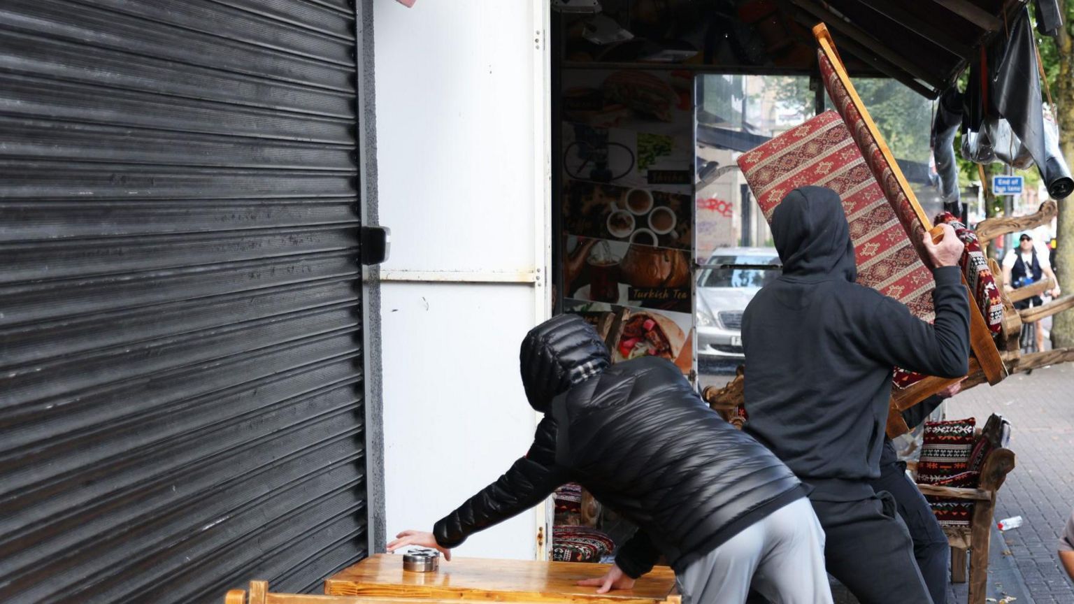 People lifting furniture outside a business and smashing windows with it